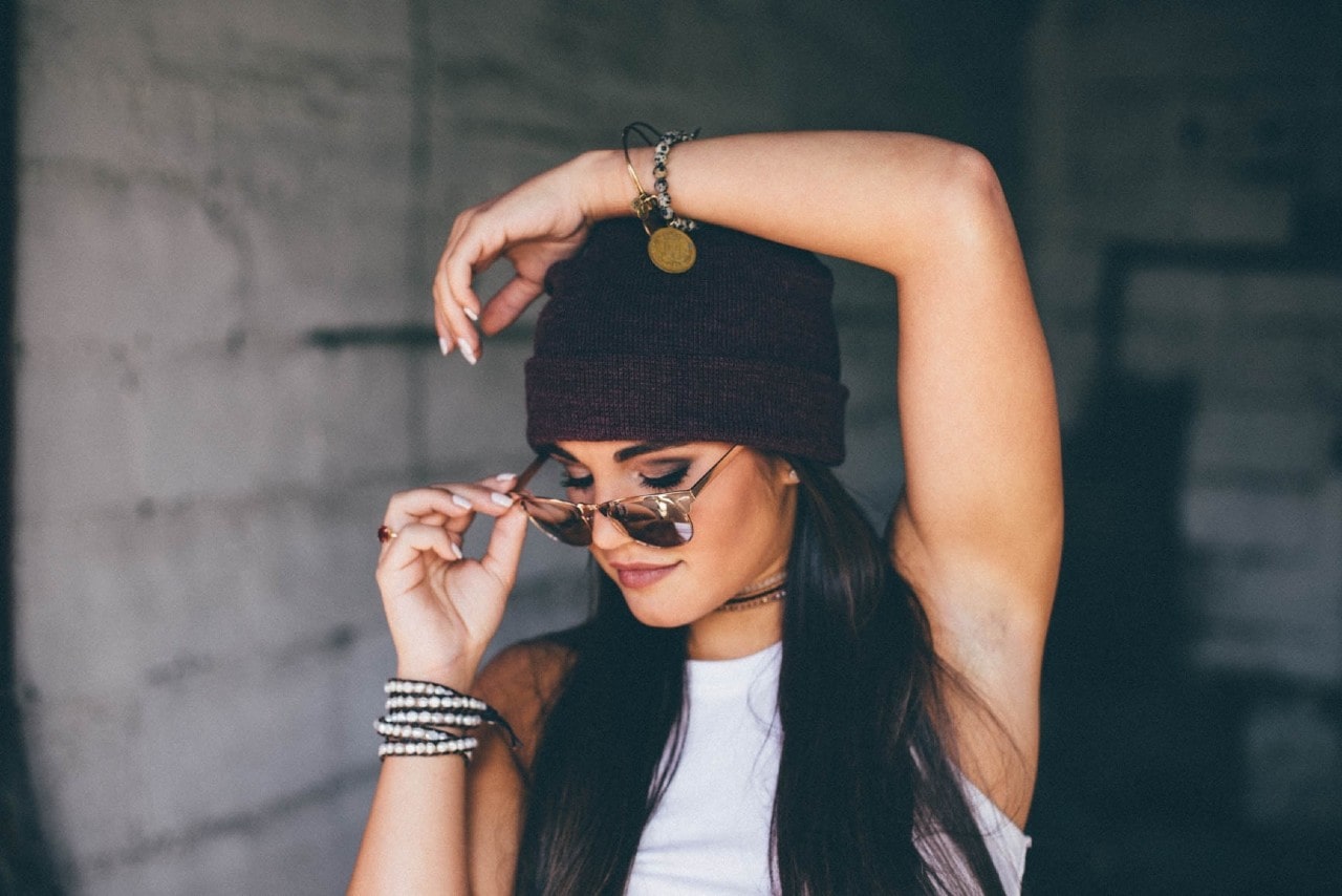 A woman wearing sunglasses and a beanie sports a variety of designer bracelets.