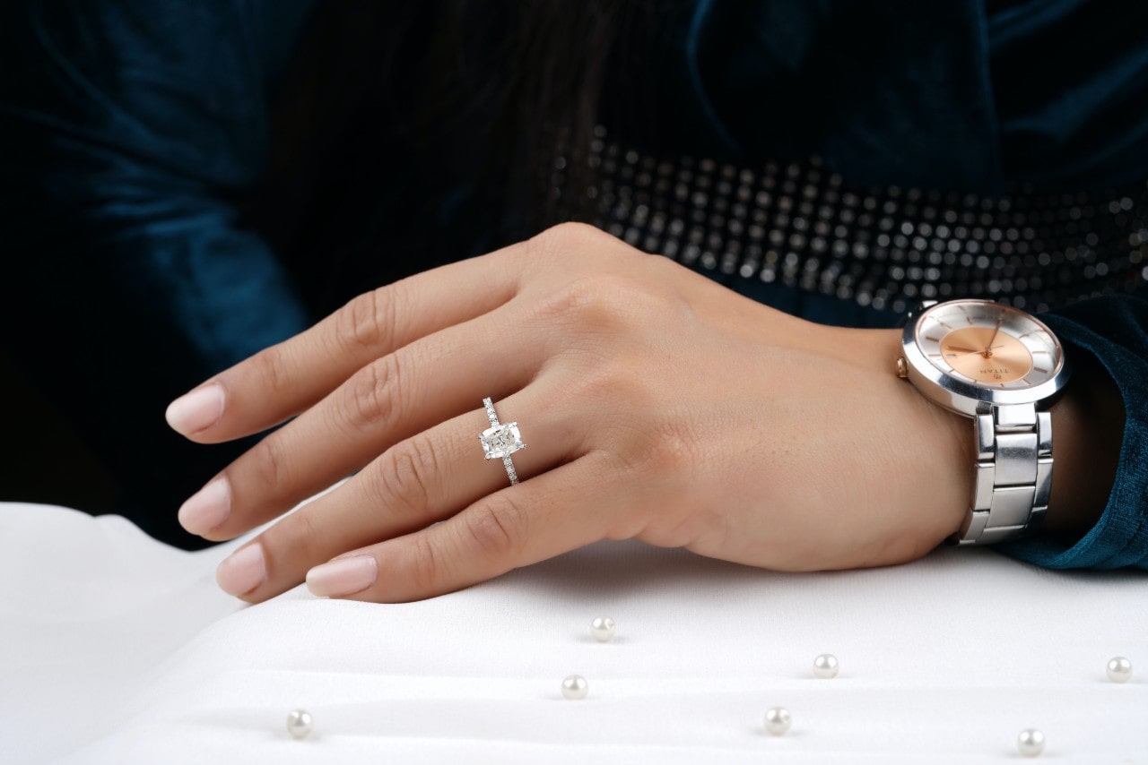 a person’s hand resting on a white surface and wearing a white gold emerald cut engagement ring