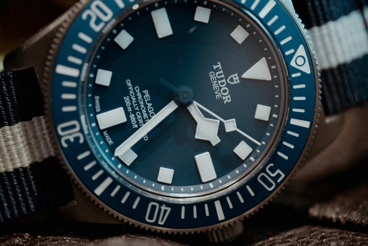 A close-up of a TUDOR Pelagos watch with a fabric strap, a blue dial, and a blue bezel.
