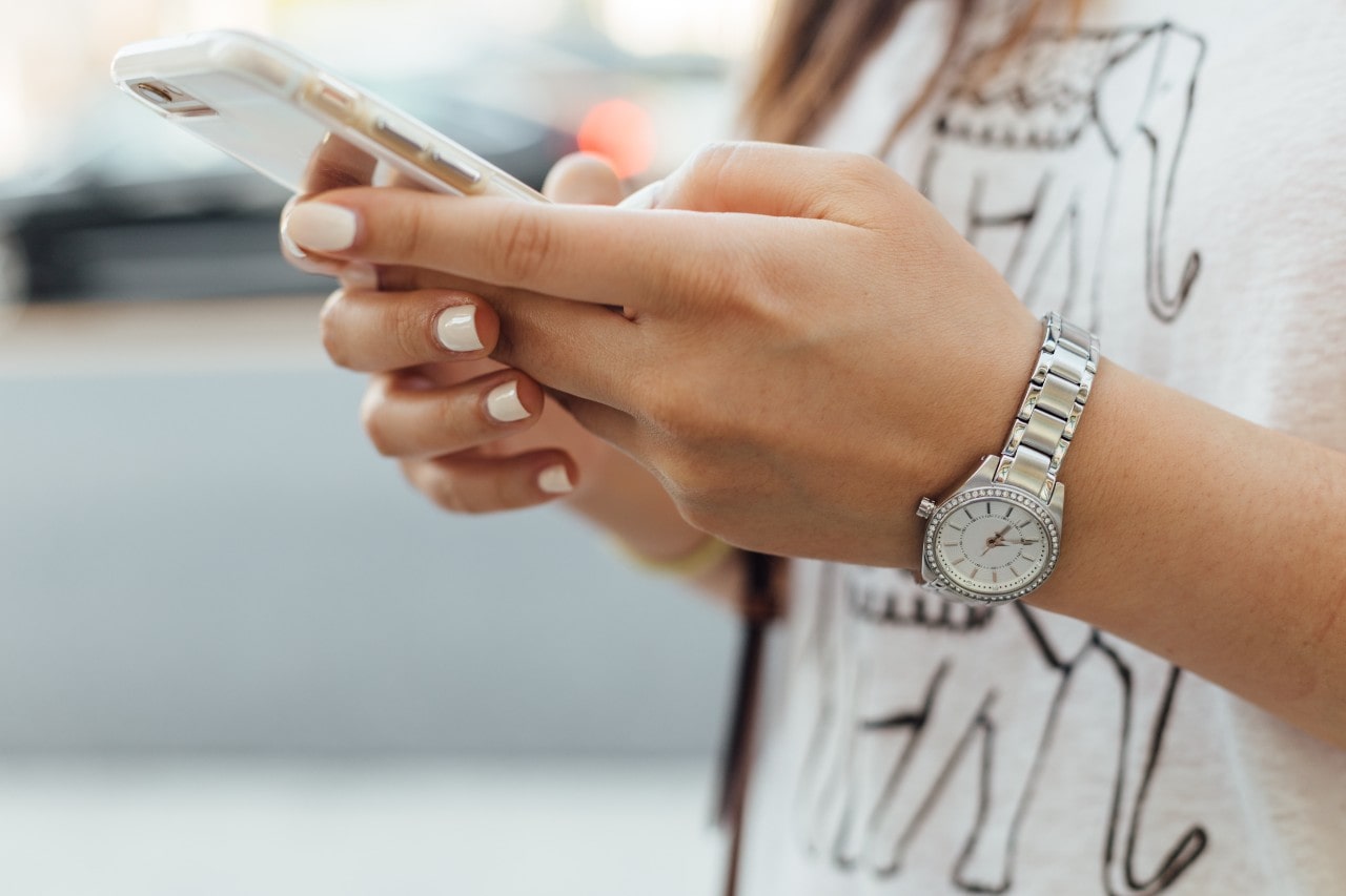 close-up image of a woman looking down at her phone and wearing a silver watch with a diamond-studded bezel