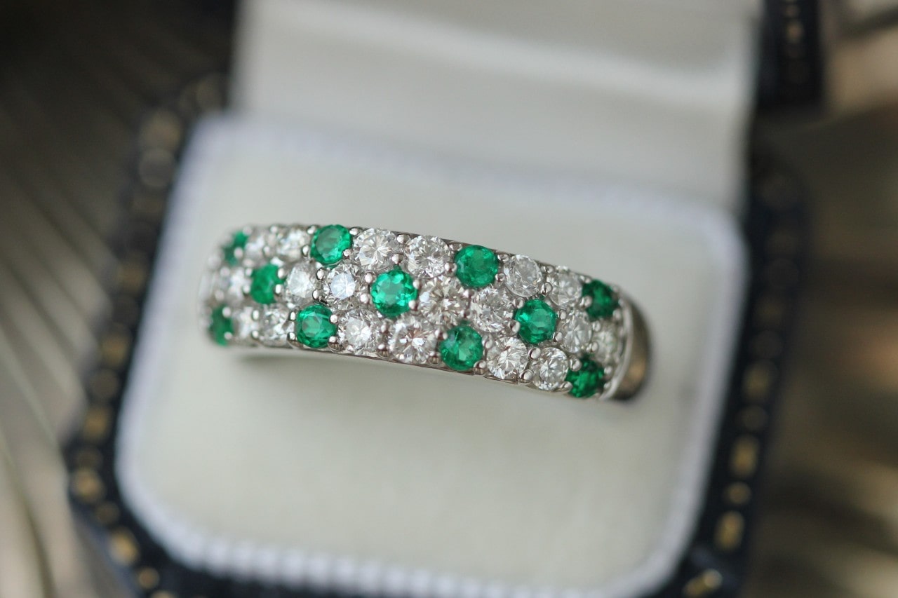 a pave wedding band featuring emeralds and diamonds in a ring box.