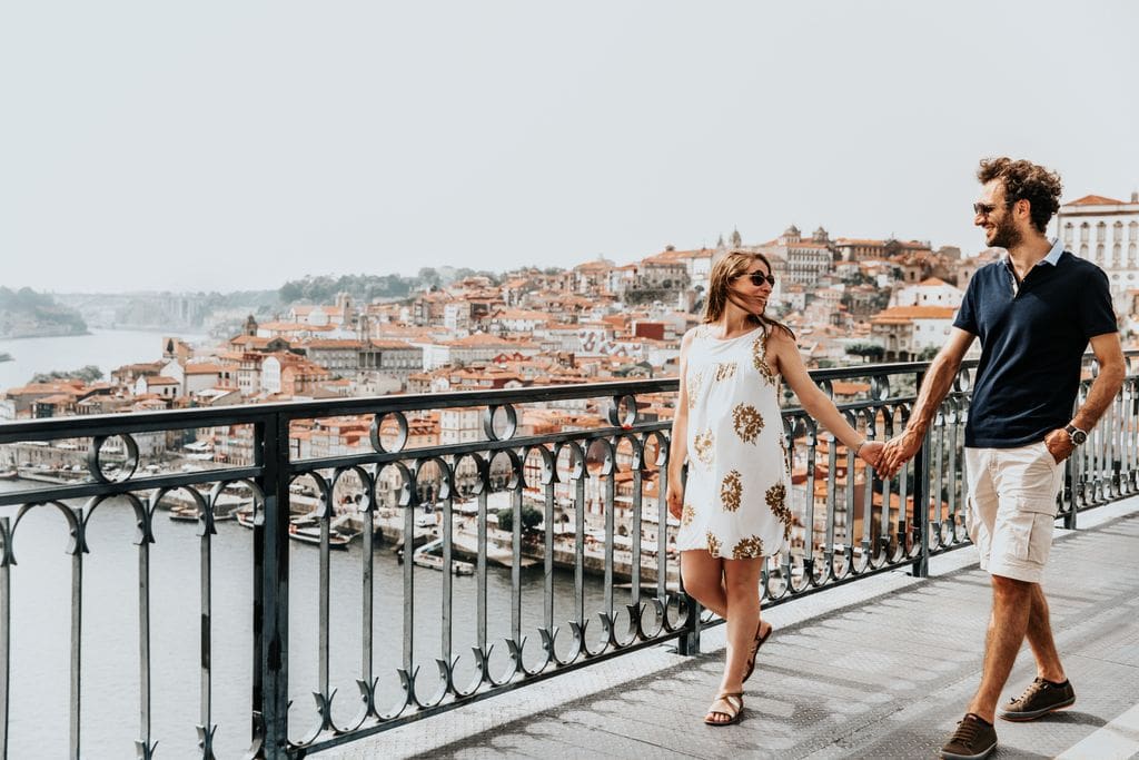 a couple walking on a bridge over a river and holding hands.