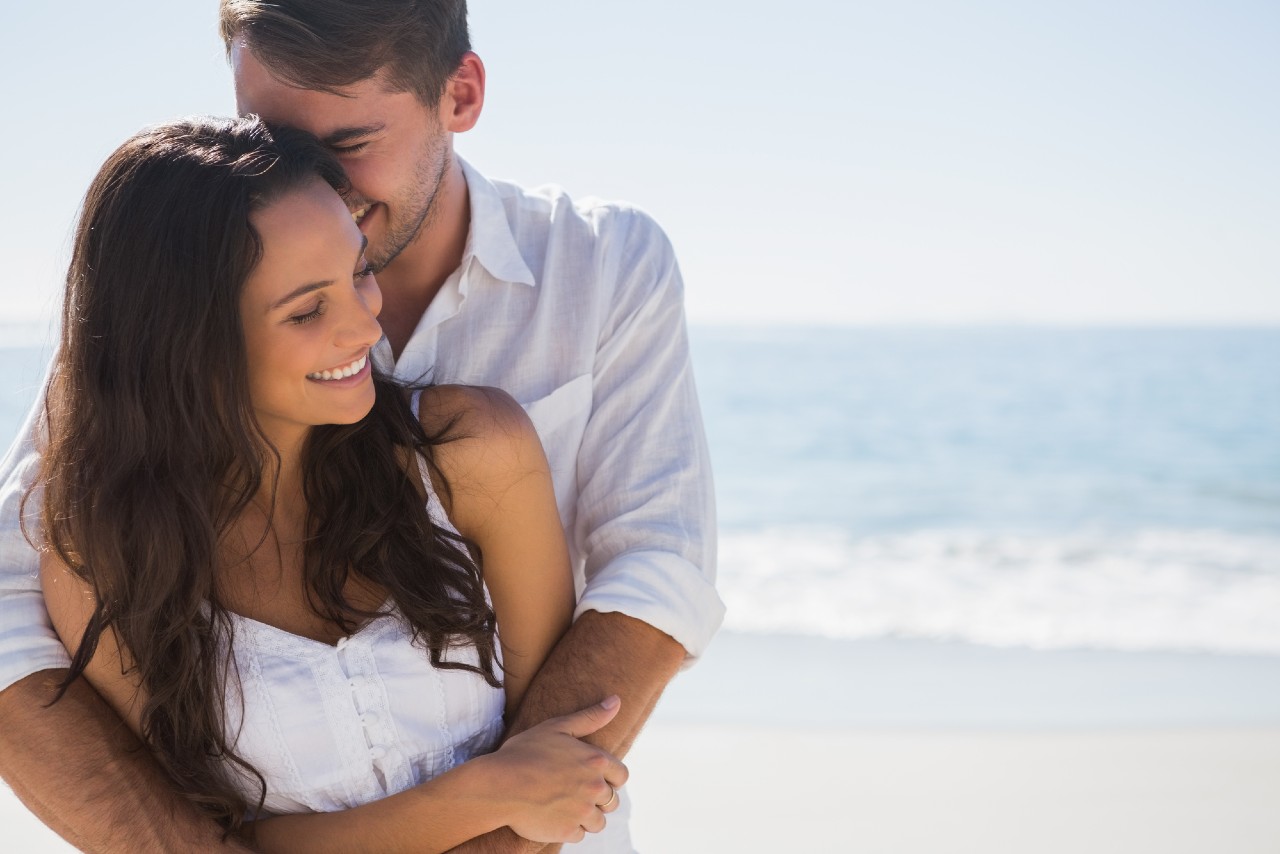 a couple embracing on the beach and wearing white