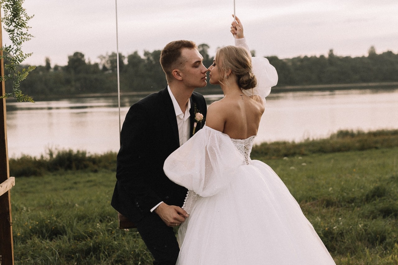 a bride and groom on a swing by a lake