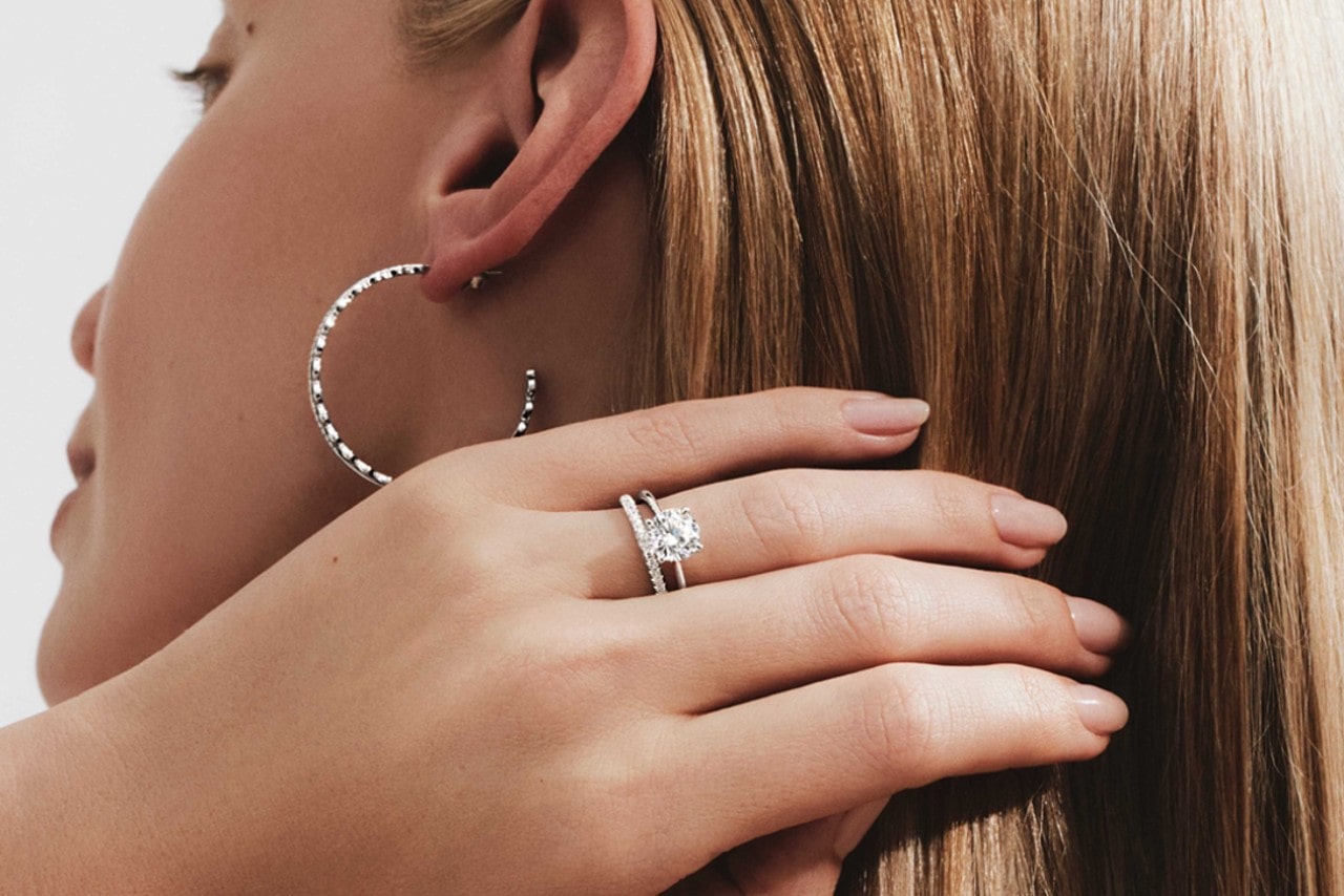 A woman brushing her hair back and showing off a solitaire diamond with an eternity wedding band