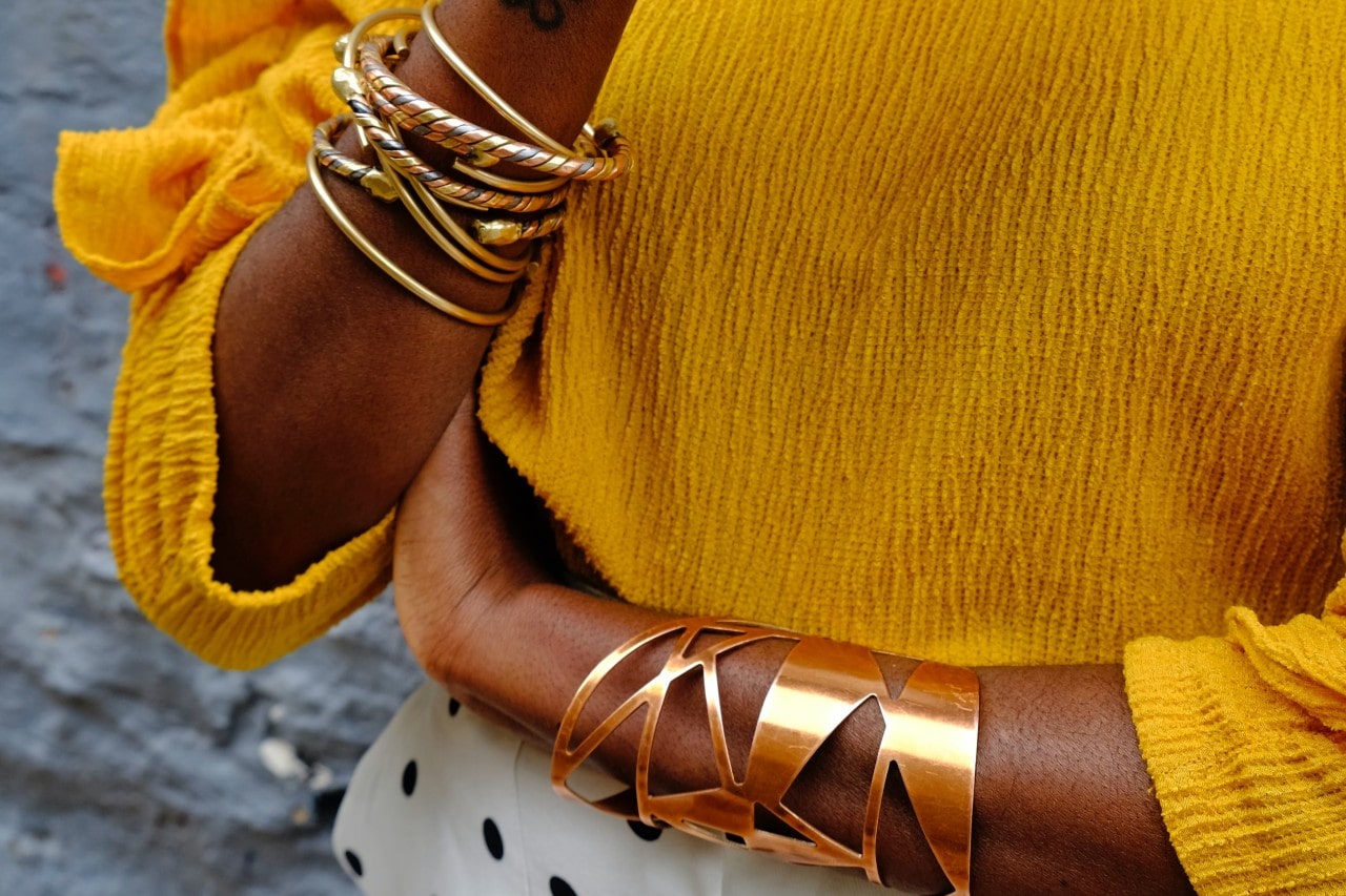 A woman in a yellow top wears a variety of glamorous gold bracelets.