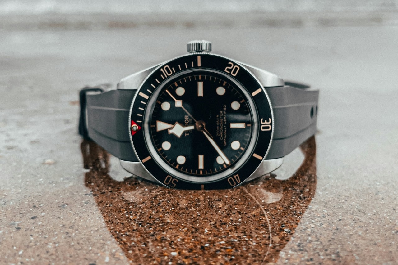 A close-up of a TUDOR watch displayed on its side on a slick graphite surface.