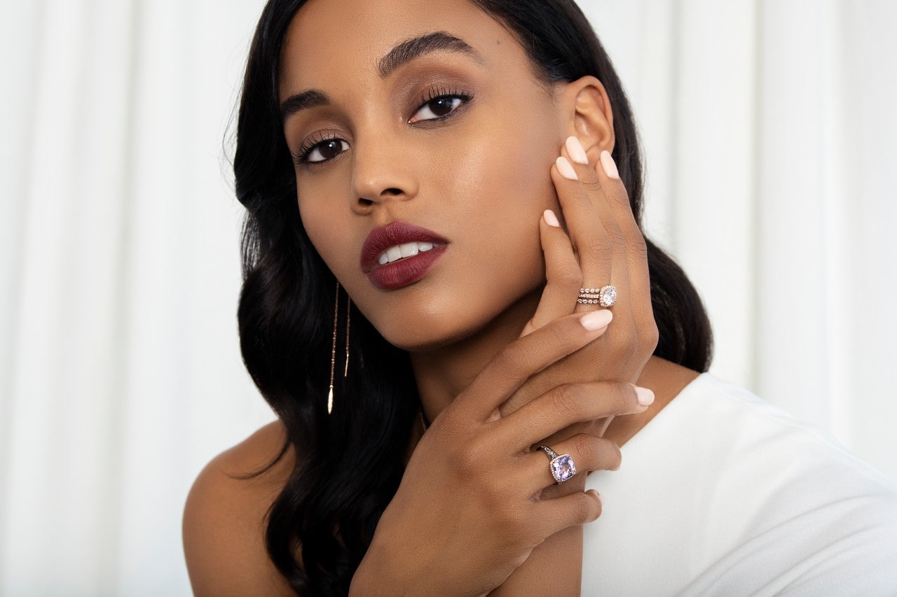 a woman holding her hand up to her face, wearing TACORI fashion rings and drop earrings