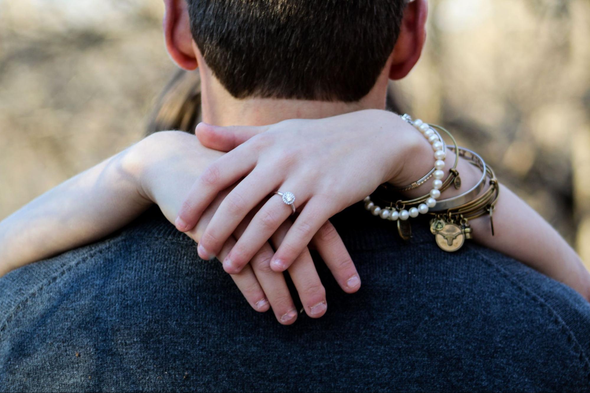A woman embracing her fiance wears a pearl bracelet with stacks of bangles.
