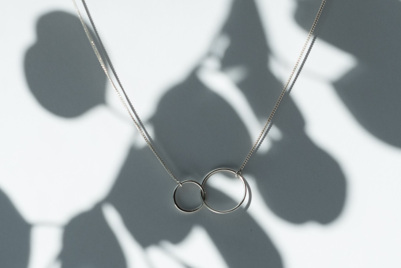 A pair of interlocking circles are attached to a silver rolo chain necklace while hanging outside.