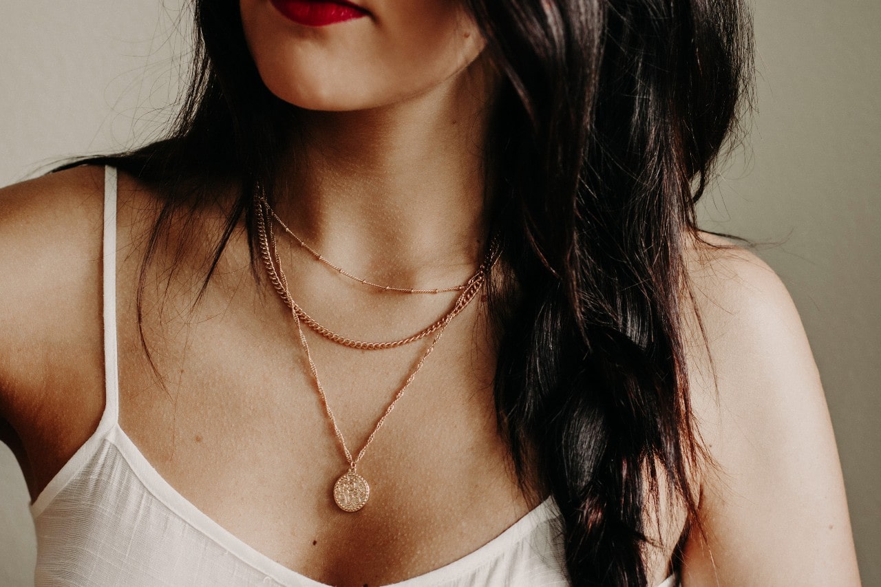 A woman wears chain necklaces with a yellow gold circle coin necklace.