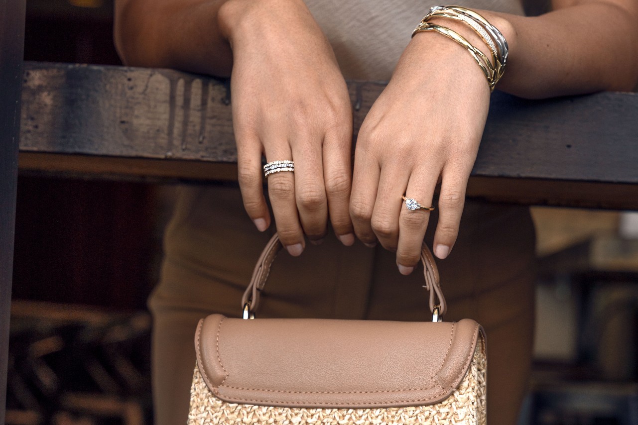 Yellow and white gold diamond bangles by TACORI along with a yellow gold solitaire engagement ring and three diamond fashion rings on the woman’s other hand holding her purse.