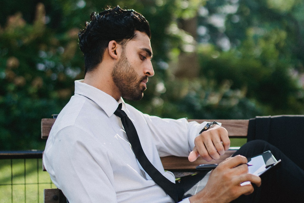 man sitting on a park bench looking at his watch